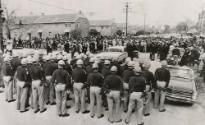 Another Day, Another Confrontation: A large crowd of demonstrators is stopped by a thin line of county police as they attempted to march to the courthouse. They were halted by Sheriff Jim Clark and told they could proceed on an individual basis if they had voter registration business there. City police later replaced the sheriff's men. A contingent of state police stands ready in foreground.
