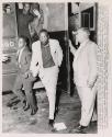 Comedian Dick Gregory (white suit-center) leaves wagon that brought him from House of Correction for court appearance here. Gregory was arrested August 12 during demonstration protesting construction of mobile classroom site. He was charged with disorderly conduct, and later refused to sign bond for his release. Handcuffed to Gregory is James Sanders, man at right is not identified
