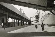 Street scene with man riding alongside boat at shipping dock, Guinea