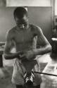 Shirtless man turning wheel to tighten clamp, Guinea