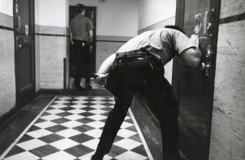 Police officer crouching in front of door in hallway during a night raid on drug pushers, NYC