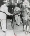 President Meets Tribal Chief: President Joseph Kasavubu of the Congo shakes hands with a scantily clad tribal chief during visit last week to Coquilhatville, capital of the Congo's Equator Province. Man in center in unidentified. Kasavubu witnessed a display of folk dancing