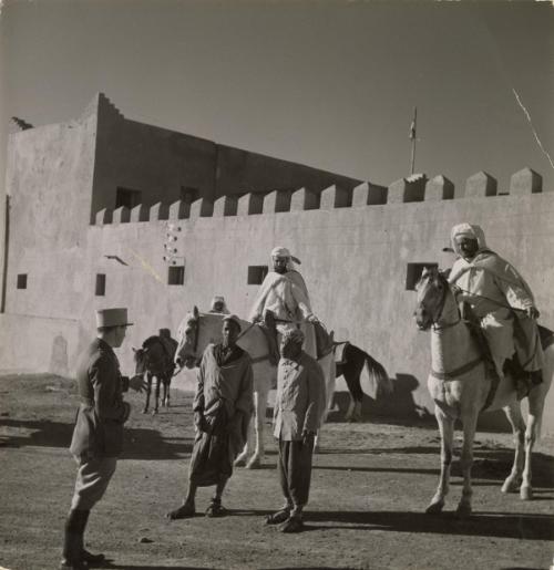 Proconsuls of France: Wide areas of France's African empire are governed practically single-handed by highly capable and experience officers, who are military commanders, administrators, judges and advisors -- all in one. A district so governed is Ouarzazate in the South of French Morocco. / In front of the fortified post, which also houses the Ministry for Native Affairs, the "proconsul-administrator" of the district, Captain Fournier, is seen talking to natives. Note also mounted native soldiers on sentry duty before the fortress, Ouarzazate, Morocco