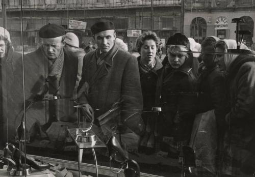 Jerusalem Alley, A Symbolic Warsaw Street: when Soviet and Polish troops met in Warsaw on January 17, 1945, it was in Jerusalem Alley that they met. At that time, Warsaw was 95% destroyed and this street, like the rest, was like a cemetery in the city of the dead. But today, 15 years later, the scene has changed considerably. There are still a few ruins to be seen, true, but for the most part, the street has been entirely rebuilt. Most of the older buildings are in the grimly-blunt Soviet-style of architecture; but in more recent structures, even this changed. And since the October 1956 revolution, a new wind of dignity and freedom has blown down the street. It is no longer an eastern city, nor is it entirely a western one. But one thing is certain, it is Polish. Pictured: a shoe store window draws a big crowd in goods hungry Warsaw.