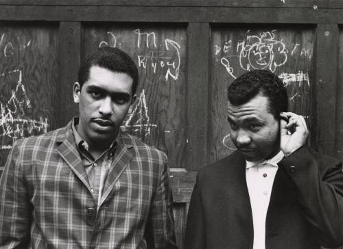 Gang Series (two men in front of wood wall of graffitti) 
