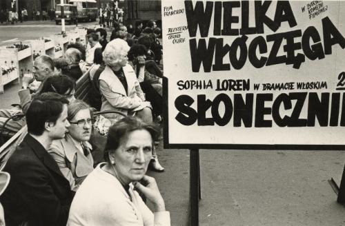 People seated at bench by poster, Katowice, Poland