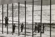 Men climbing fence with rocky hill in the background, South Africa