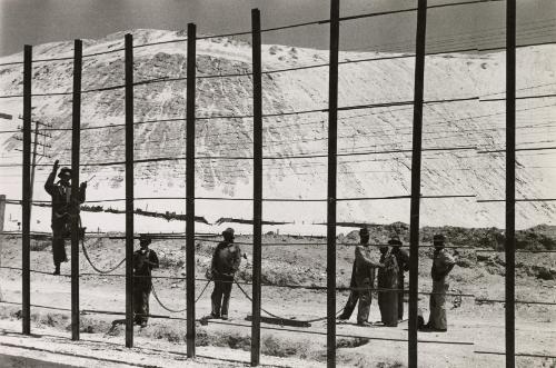 Men climbing fence with rocky hill in the background, South Africa