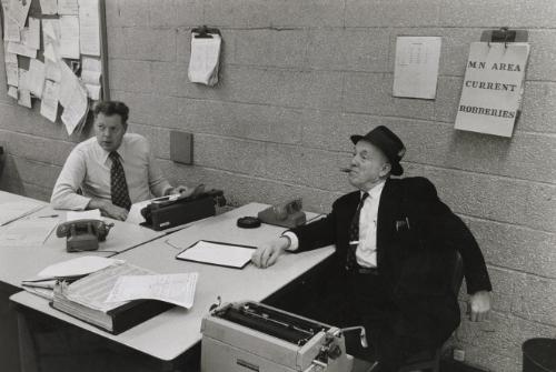 A retired policeman (seated in dark suit and hat) returns to the police station to check up on the detectives' day to day work, NYC