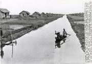 Canal Does Double Duty: A small boar is maneuvered along a canal in the Cai San area of South Viet Nam where thousands of acres of abandoned land have been reclaimed through the American aid program. This canal, while serving as a transportation route, also provides water for rice planting. The area is included in the resettlement program that has benefited some 12,000 refugee families from communist North Viet Nam, Cai San, South Viet Nam