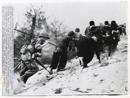 Vietnam Shepard: Carrying a walking stick over his shoulder and his M16 rifle in his hand, a soldier of the U.S. 25th Infantry Division herds a group of Vietnamese families to a helicopter landing zone for interrogation. The Vietnamese were rounded up after a brief firefight at a village near Duc Pho, about 325 miles north of Saigon, during a search and clear operation