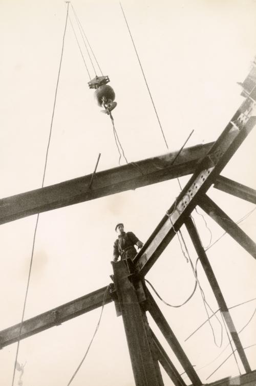 Construction worker supervising iron beam placement while standing on high beams
