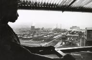 Partly silhouetted figure looking at factory in background, Guinea