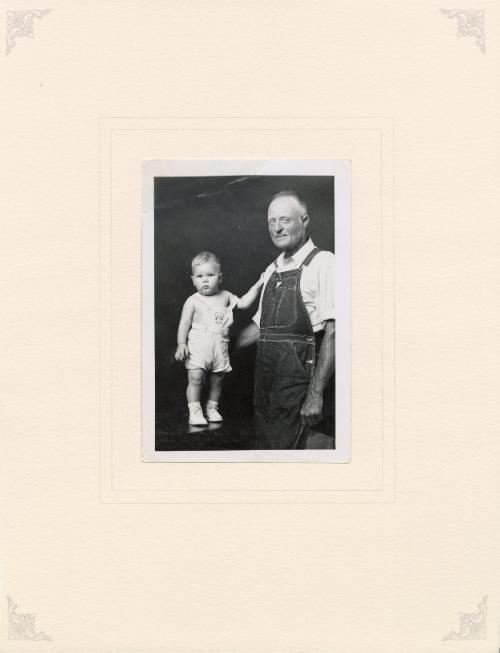 Standing grandfather and infant, both in overalls