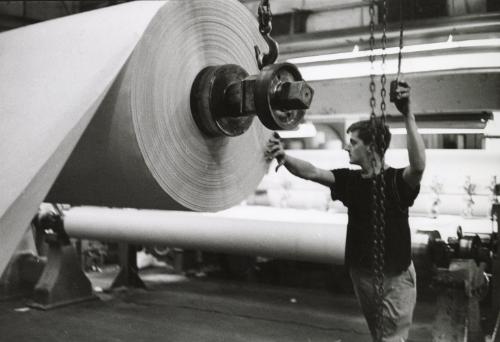 Man moving roll of paper into place on printing press, Quebec