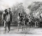 Burden Of War: Carrying youngsters nearly their own size, Laotian youths trudge barefooted down a dusty jungle road while fleeing the battle zone in the Plain of Jars. They were among refugees who arrived at the outpost of Borikhane in central Laos after walking more than 75 miles and evacuating their homes before the onslaught of invading Communist Pathet Lao troops, Laos.