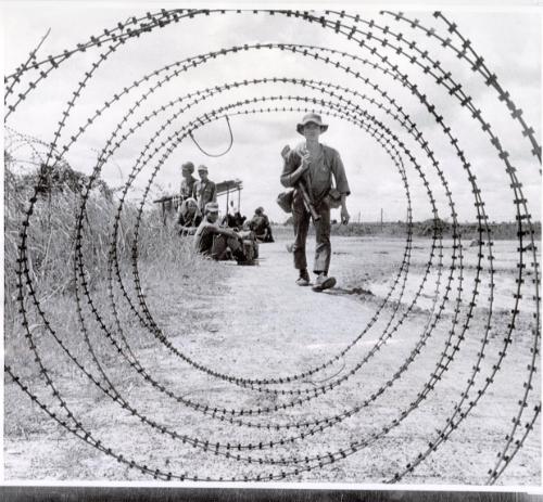 A South Vietnamese militiaman is framed in a coil of razor wire, similar to barbed wire, at an outpost near Cu Chui in the Saigon region. Military patrols have continued in the post cease-fire days.