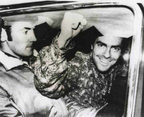 Ordered to Leave England: "Yippie" leader Jerry Rubin makes clenched fist salute as he's taken in police car, escorted by a Special Branch detective, here November 13th, Rubin and a companion, Stewart Albert, have been advised they will be deported unless they leave Britain voluntarily.