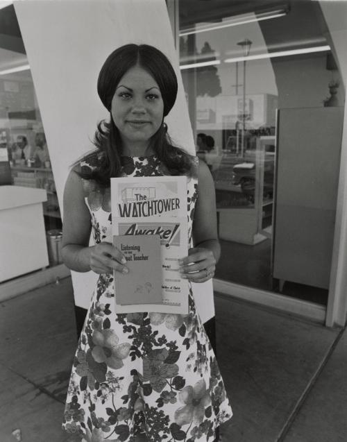My witness is here for Jehovah. Usually people walk by, but if you catch someone's eye they will stop and take the magazine. Livermore, California 1973
